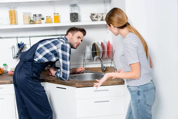 Young woman gesturing near handyman leaning on sink in kitchen — Stock Photo