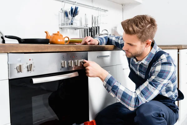 Giovane tuttofare girando il pulsante del forno in cucina — Foto stock