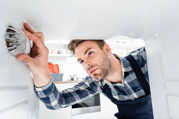 Handyman focado verificando o congelador no primeiro plano borrado na cozinha — Fotografia de Stock