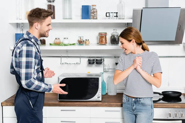Jovem alegre com as mãos apertadas olhando para microondas fixa perto de faz-tudo na cozinha — Fotografia de Stock