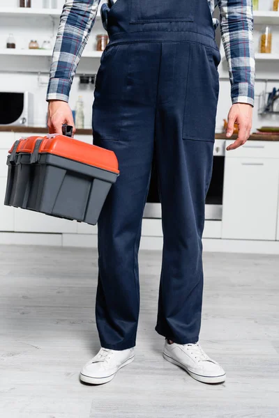 Cropped view of young handyman holding toolbox with blurred kitchen on background — Stock Photo