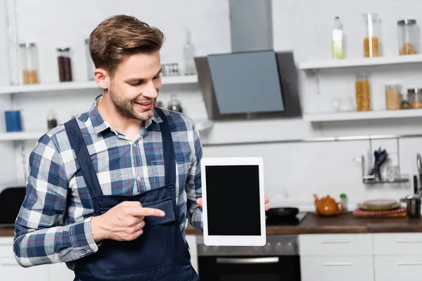 Reparador feliz apuntando con el dedo a la tableta con cocina borrosa en el fondo - foto de stock