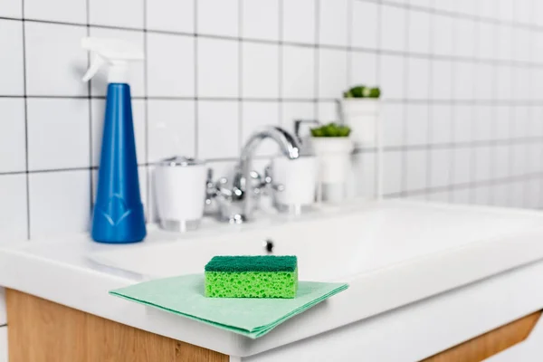 Sponge on rag near detergent on bathroom sink on blurred background — Stock Photo