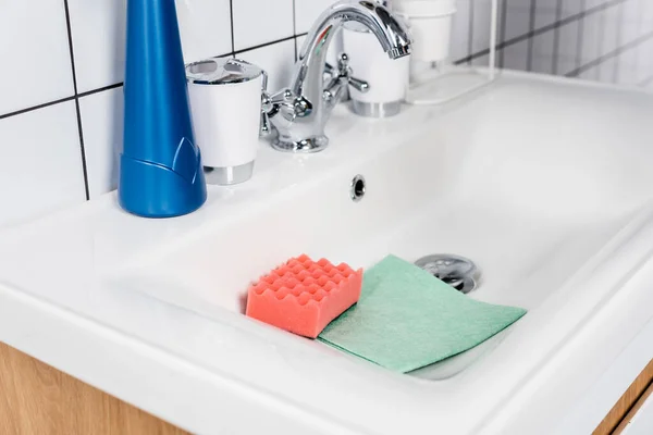 Sponge and rag in sink near faucet in bathroom — Stock Photo