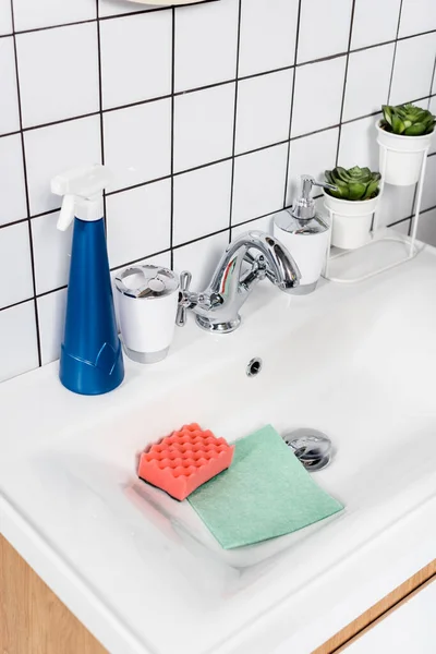 Бутылка моющего средства возле губки и тряпка в раковине в современной ванной комнате — стоковое фото
