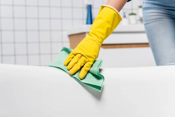 Vista recortada de mujer en guante de goma bañera de limpieza con trapo en el baño - foto de stock