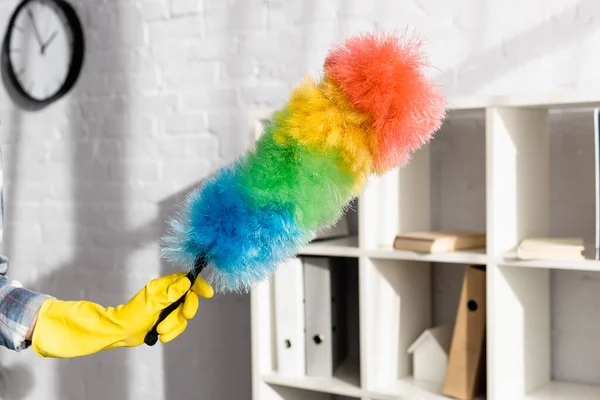 Cropped view of woman in yellow rubber glove holding colorful dust brush at home — Stock Photo