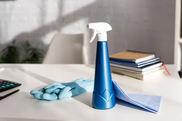 Detergent, rag and rubber gloves near notebooks on blurred background on table — Stock Photo