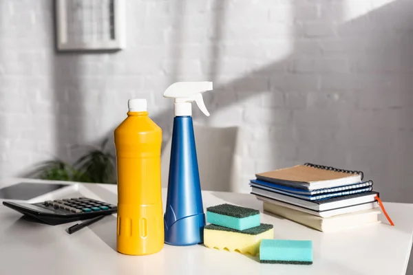 Bottles of detergents and sponges near notebooks and calculator on table — Stock Photo