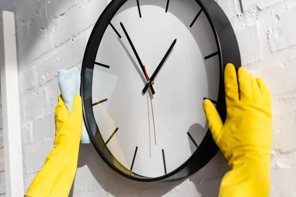 Vue recadrée de la personne dans des gants en caoutchouc horloge de nettoyage avec chiffon sur le mur à la maison — Photo de stock