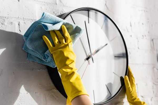 Vista cortada da mulher em luvas de borracha relógio de parede de limpeza com pano — Fotografia de Stock