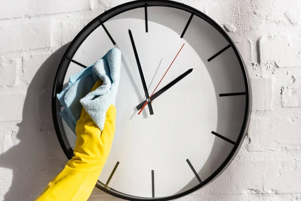 Cropped view of person in rubber glove cleaning clock with rag on white brick wall — Stock Photo