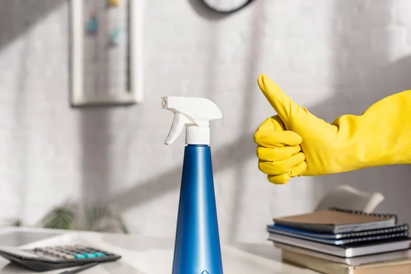 Vista cortada da mão em luva de borracha mostrando polegar para cima perto de detergente na mesa — Fotografia de Stock