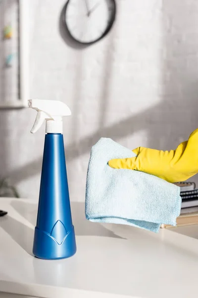 Cropped view of hand in rubber glove holding rag near bottle of detergent on table — Stock Photo