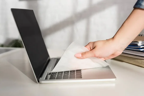 Cropped view of woman cleaning laptop keyboard with napkin near notebooks on table — Stock Photo