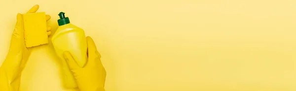 Top view of hands in rubber gloves holding sponge and dishwashing liquid on yellow background, banner — Stock Photo