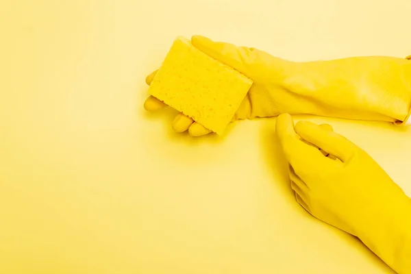 Vista ad alto angolo delle mani in guanti di gomma che tengono spugna su sfondo giallo — Foto stock