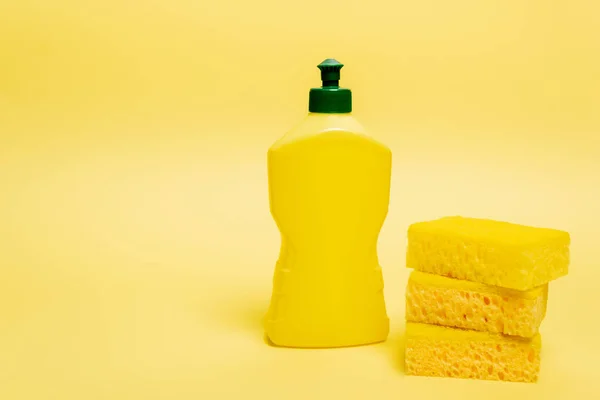 Éponges jaunes et bouteille de liquide vaisselle avec bouchon sur fond jaune — Photo de stock