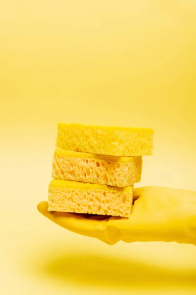 Vista cortada da mão em luvas de borracha segurando esponjas no fundo amarelo — Fotografia de Stock