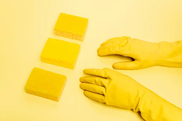 Высокий угол обзора человека в резиновых перчатках и губках на желтом фоне — стоковое фото