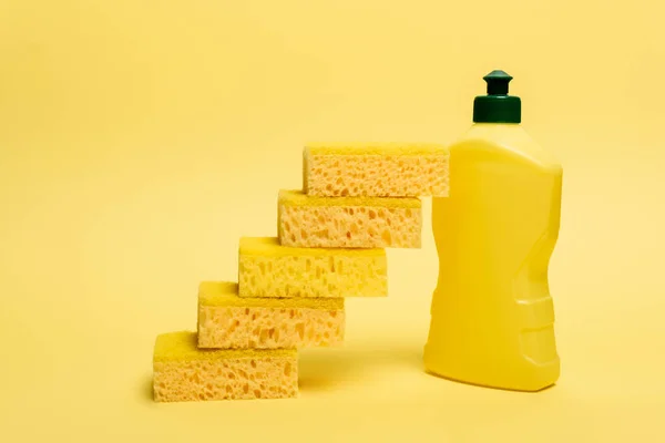Губки біля жовтої пляшки посудомийної рідини на жовтому фоні — стокове фото
