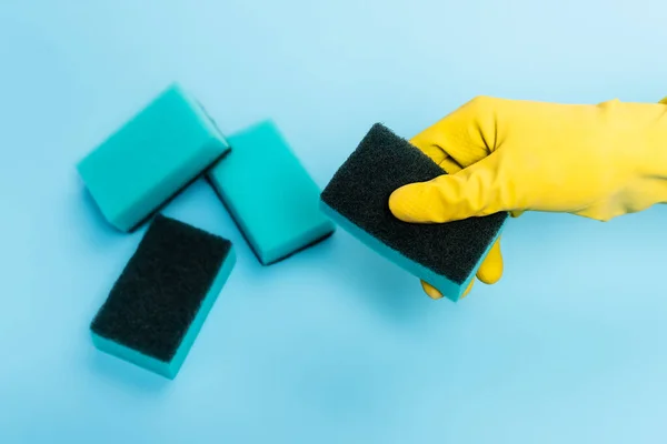 Vista superior da mão na luva de borracha segurando esponja no fundo azul — Fotografia de Stock