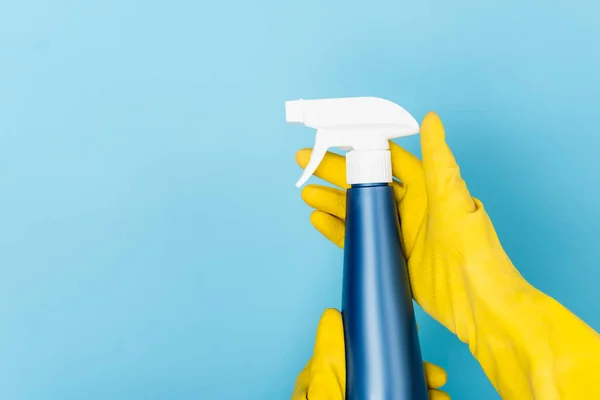 Vista cortada das mãos em luvas de borracha amarela segurando detergente com pulverizador no fundo azul — Fotografia de Stock