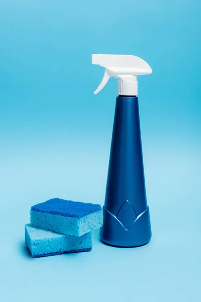 Bouteille bleue de détergent et éponges sur fond bleu — Photo de stock