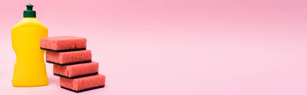 Бутылка жидкости для мытья посуды и губки на розовом фоне, баннер — стоковое фото