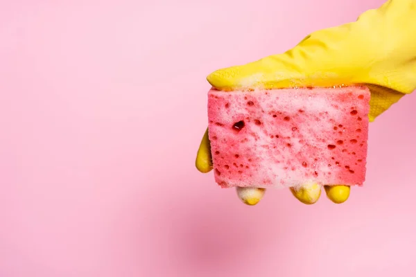 Vue recadrée de la main en gant frotté tenant éponge avec mousse de savon sur fond rose — Photo de stock