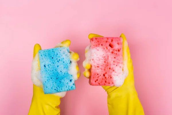 Top view of hands in rubber gloves holding sponges with soap foam on pink background — Stock Photo