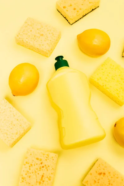 Vue du dessus du liquide vaisselle, des éponges et des citrons sur fond jaune — Photo de stock