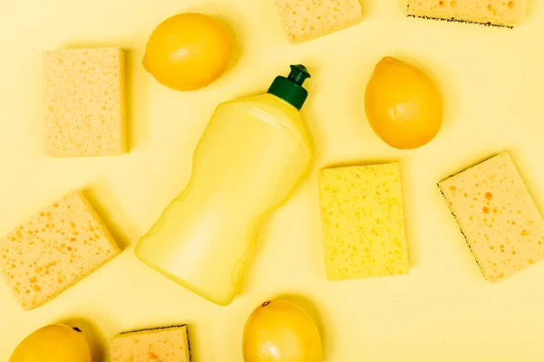 Vista superior de limones enteros cerca de esponjas y líquido lavavajillas sobre fondo amarillo - foto de stock