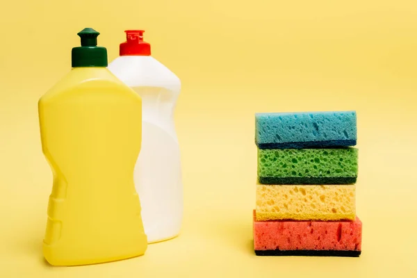 Bottles of dishwashing liquid and colorful sponges on yellow background — Stock Photo