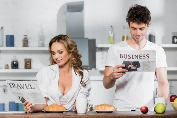 Sexy woman reading travel newspaper near boyfriend, coffee and breakfast in kitchen — Stock Photo