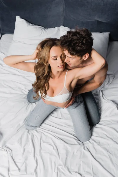 Overhead view of shirtless man touching seductive girlfriend in bra and jeans on bed — Stock Photo