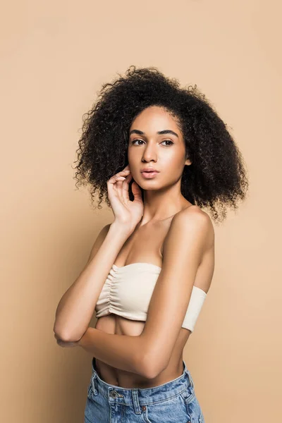 Rizado joven afroamericana mujer con los hombros desnudos mirando hacia otro lado en beige - foto de stock