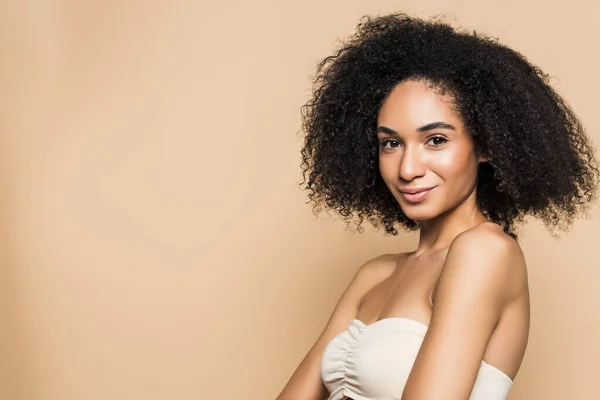 Pretty african american woman with bare shoulders looking at camera isolated on beige — Stock Photo