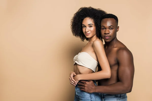 Sin camisa afroamericano hombre abrazando sonriente novia en beige - foto de stock