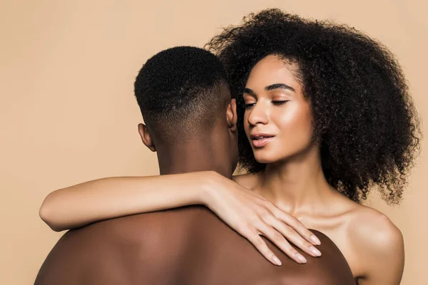 Encaracolado afro-americano mulher abraçando namorado sem camisa isolado no bege — Fotografia de Stock