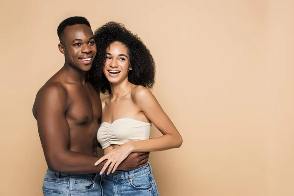 Happy african american woman laughing and hugging with cheerful boyfriend isolated on beige — Stock Photo