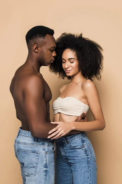 Hombre afroamericano abrazando a mujer con los ojos cerrados en beige - foto de stock