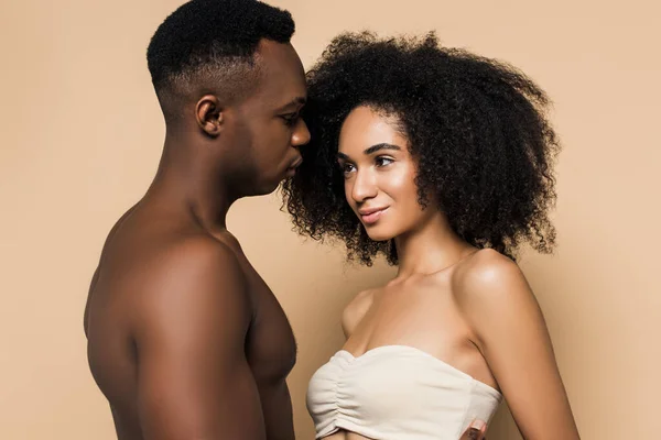 Hombre afroamericano sin camisa mirando a la mujer rizada en la parte superior aislado en beige - foto de stock