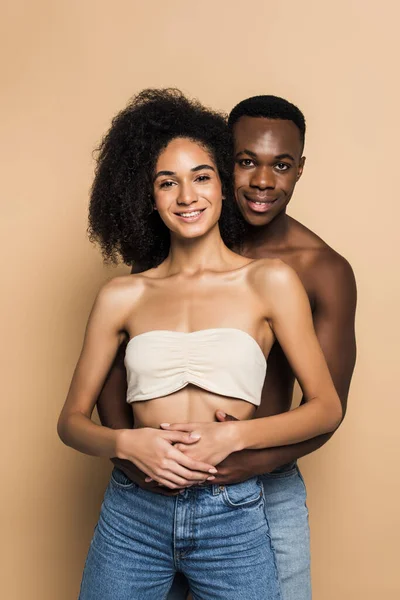 Joyful african american woman and man smiling while hugging on beige — Stock Photo