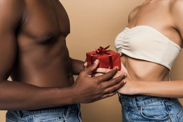 Vue recadrée d'un homme afro-américain torse nu offrant un cadeau enveloppé à une femme isolée sur beige — Photo de stock