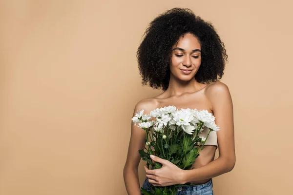 Feliz afro-americana segurando flores isoladas no bege — Fotografia de Stock