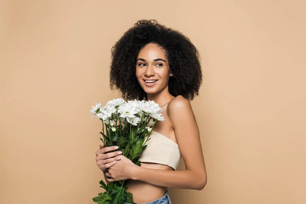 Alegre mujer afroamericana sosteniendo flores aisladas en beige - foto de stock