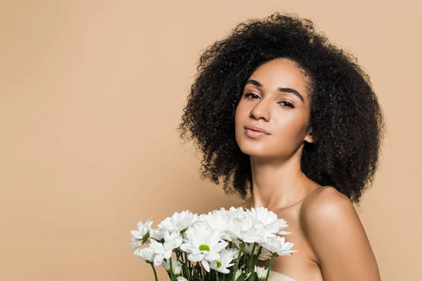 Curly african american woman with bare shoulders near flowers isolated on beige — Stock Photo