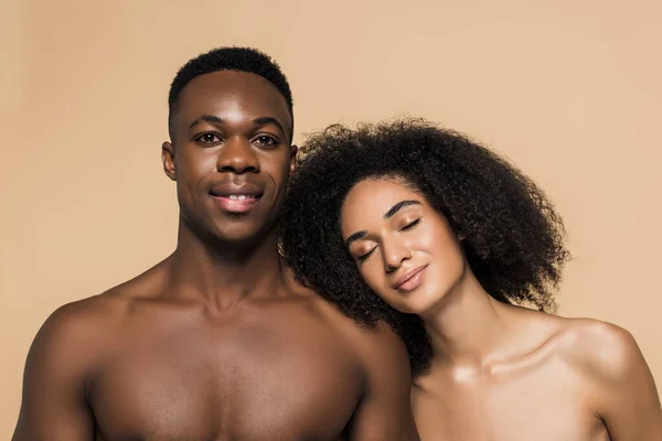 Curly african american woman with bare shoulders leaning on happy boyfriend isolated on beige — Stock Photo