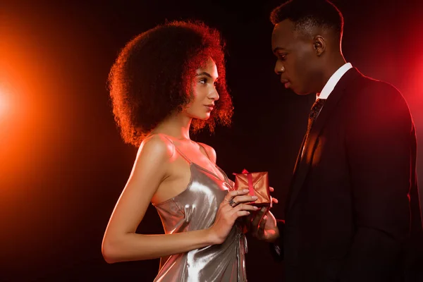 Side view of african american man giving present to woman in dress on black — Stock Photo